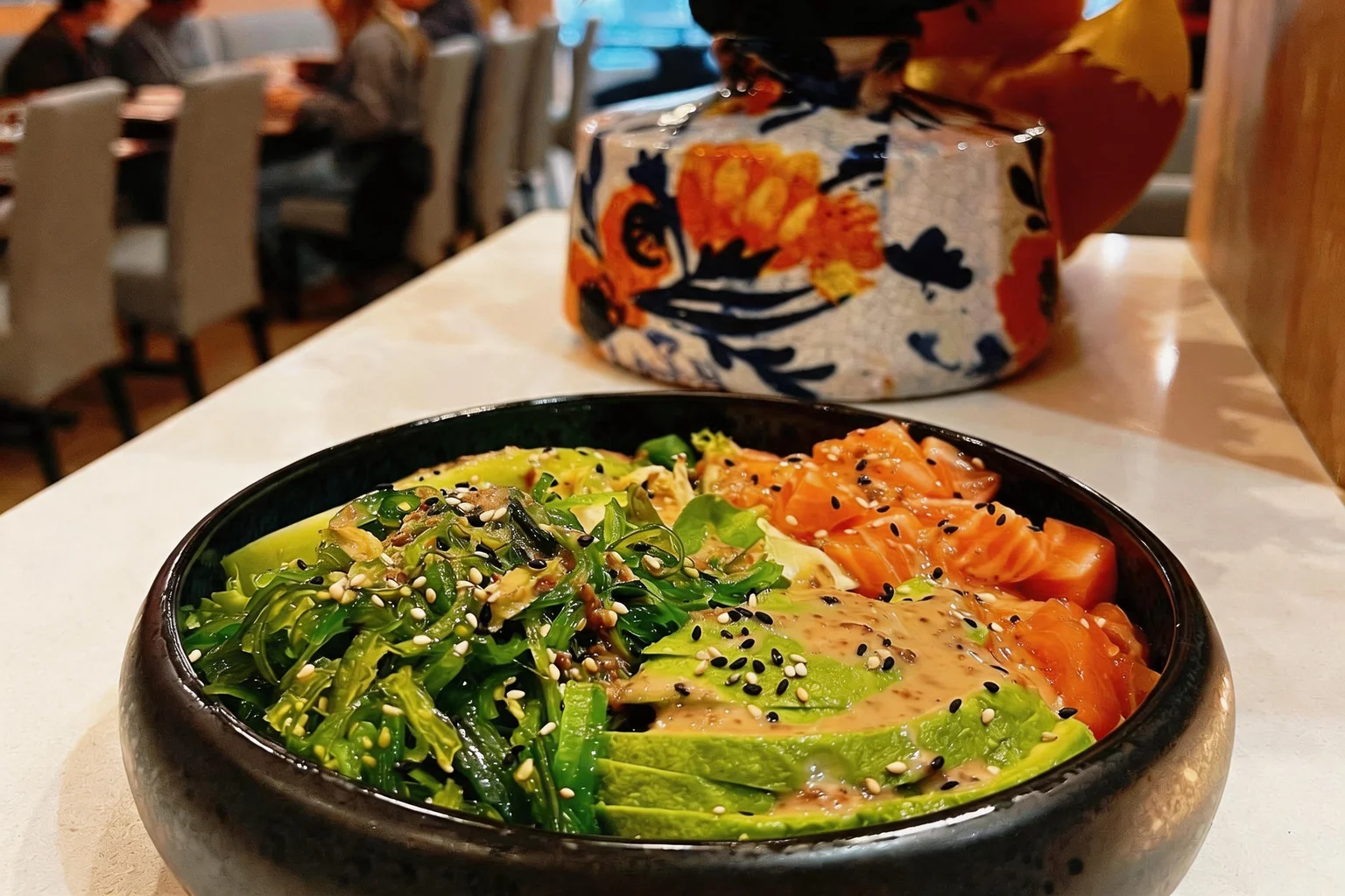Black bowl with diced raw salmon, avocado and seaweed salad.