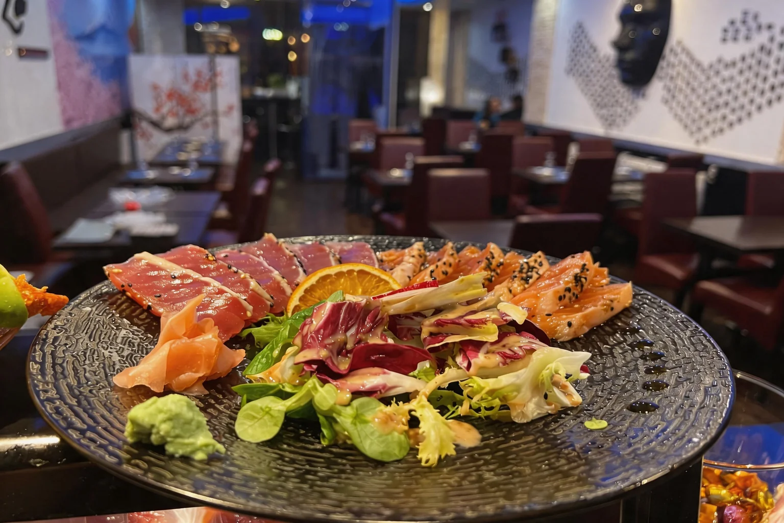 Oval platter with slices of seared tuna and salmon, an orange slice, pickled ginger, wasabi and red radicchio salad.