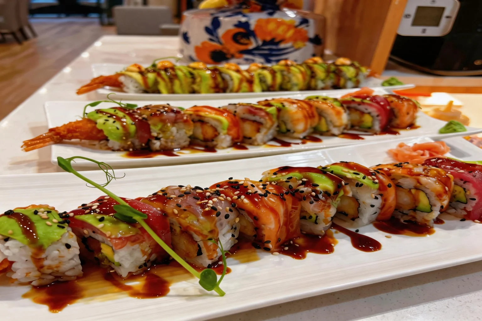 Three white platters of assorted sushi rolls, drizzled with sauce.